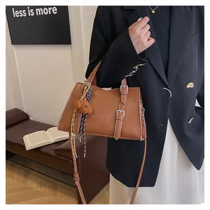 Detail of brown leather tote bag featuring metal buckles and a cute plush bear charm