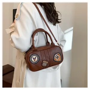 Brown vintage square bag with military patches and adjustable strap on a white coat