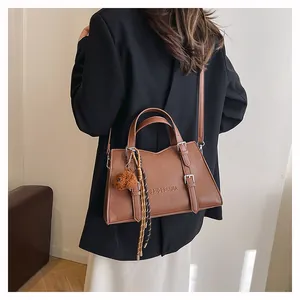 Detail of brown leather tote bag with metal buckles and a cute plush bear charm decoration