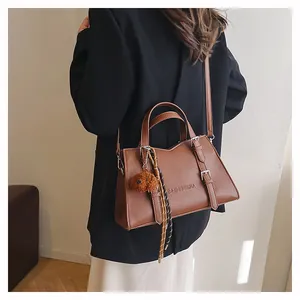 Detail of brown tote bag with bear charm and decorative ribbon in use on shoulder