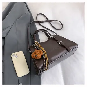 Detail of dark brown leather tote bag with metallic buckles and plush bear charm decoration