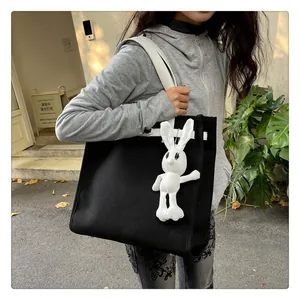 Detail of minimalist black canvas tote bag with white trim and plush rabbit charm