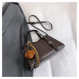 Detail of dark brown faux leather tote bag with decorative straps and puppy charm