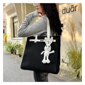 Close-up of canvas tote bag featuring Kelly buckle and white plush rabbit charm detail