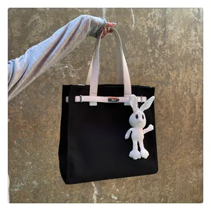 Close-up of black canvas tote with Kelly lock, contrast straps, and rabbit charm