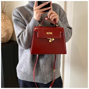 Détail élégant de sac à main en cuir rouge vin classique avec serrure dorée et poignée.