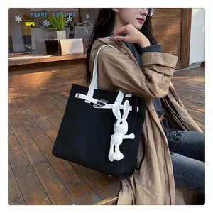 Detail of black canvas tote bag featuring metal clasp and white plush rabbit charm