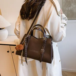 Classic dark brown leather tote bag with a teddy bear pendant on a female model