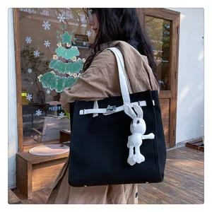 Macro detail of black canvas tote bag with white strap, metal turn lock, and rabbit pendant