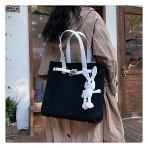 Close-up of black canvas tote bag with white leather straps and turn-lock detail