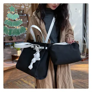 Detail of black canvas tote bag with contrast white handles and cute plush bunny charm