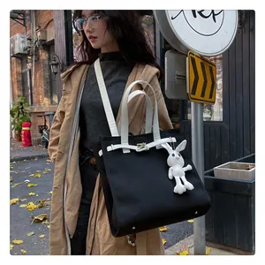 Detail of black canvas tote bag featuring white handles and a plush bunny charm on a model