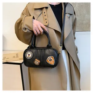 Detail of black faux leather bag featuring retro embroidered patches and gold hardware