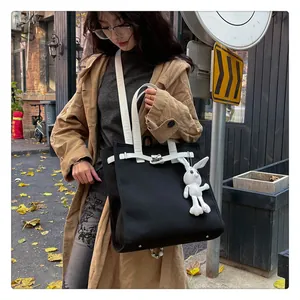 Close-up of black canvas tote bag with white strap detail and cute rabbit plush charm