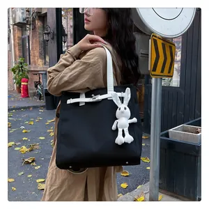 Detail of a black canvas tote with Kelly buckle, white handles, and a rabbit plush charm