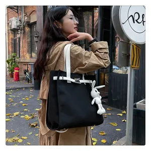 Detail of black canvas tote bag with white straps and a cute plush rabbit charm