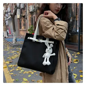 Detail of black canvas tote bag featuring white straps, metal lock, and a plush bunny charm