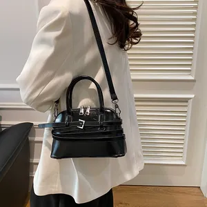 Glossy black shell bag with belt decorative buckle, handheld by model in white blazer