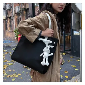 Detail of a black canvas tote with white handles and a plush bunny charm in street style