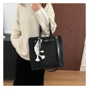 Detail of black canvas tote bag featuring leather straps and a white plush rabbit charm