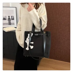 Close-up of black canvas tote bag with metal buckle and cute white bunny plush pendant