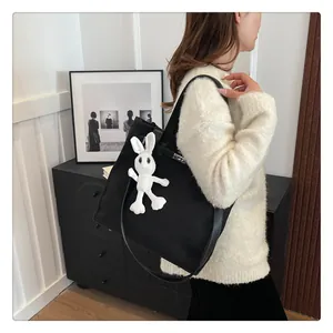 Detail of black canvas tote bag with Kelly buckle and white plush rabbit charm accessory