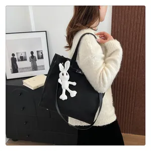 Detail of black canvas tote bag with metal buckle and cute white rabbit plush pendant