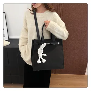 Black canvas tote bag with Kelly buckle and white rabbit plush charm worn by model