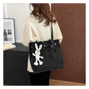 Detail of black canvas tote bag with leather handles and cute white bunny charm accessory