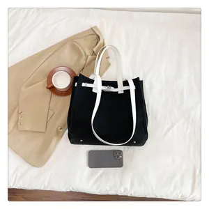 Detail view of monochrome canvas tote with metal clasp, shoulder strap, and size reference