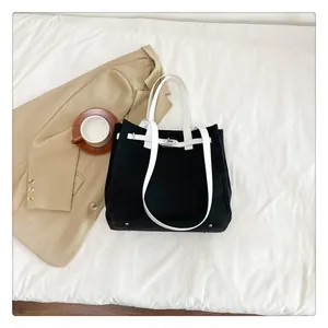Detail of canvas tote bag showing silver metal base studs and contrast white leather trim
