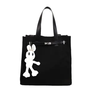 Black canvas Kelly tote bag with leather straps and a white rabbit charm keychain