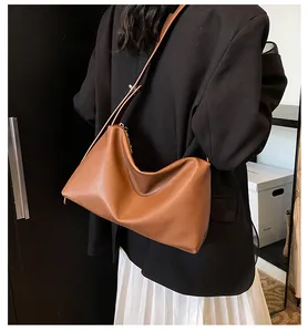 Sac hobo en cuir marron porté avec un blazer noir et une jupe plissée blanche
