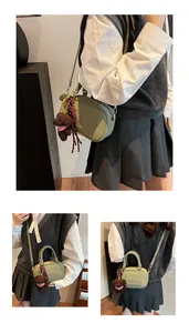 Detail of sage green box bag with embossed logo, plush bear charm and plaid ribbon accent