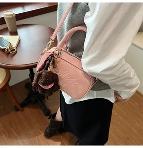 Pink matte crossbody bag with embossed logo and a dark brown plush dog charm detail