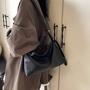 Sac à bandoulière noir vintage en similicuir souple porté par un mannequin en trench-coat