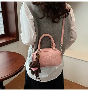 Detail of pink crossbody bag with embossed letters and a brown plush teddy bear charm