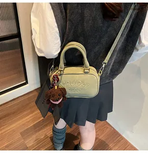 Detail of sage green suede bowling bag with embossed lettering and plush bear charm