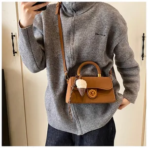 Detail van een bruine crossbodytas met gouden knopsluiting en een pluche ijsbedeltje