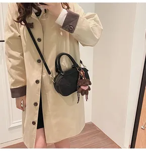 Fashionable black Boston bag with a teddy bear charm shown on a stylish trench coat