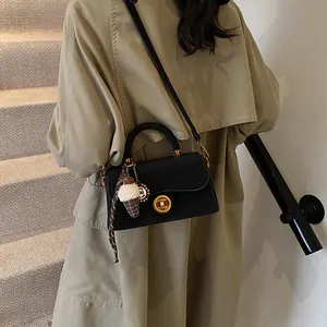 Elegante zwart mat lederen schoudertas met gouden details gedragen door model in trenchcoat