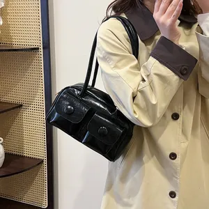 Glossy black multi-pocket shoulder bag in vintage style worn with a beige trench coat