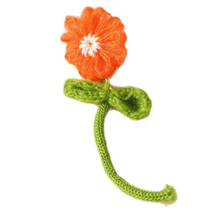 Handmade knitted orange fabric flower with green stem and leaf on white background
