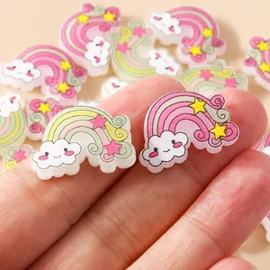Macro shot of cute resin rainbow and smiling cloud charms held between fingers for size