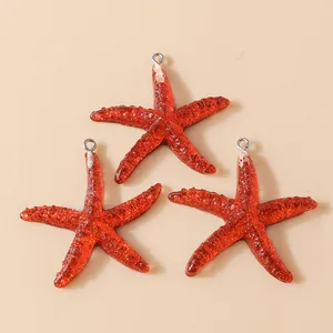 Detail view of three red resin starfish pendants with gold glitter and silver metal loops