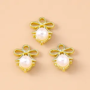 Three gold bow pendants with pearls for DIY jewelry making on a warm beige background