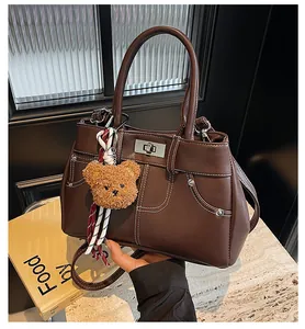 Détail d'un sac à main marron avec surpiqûres blanches, fermoir argenté et bijou ours