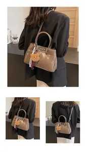 Détail d'un sac à bandoulière marron foncé avec fermoir en métal et charm d'ours