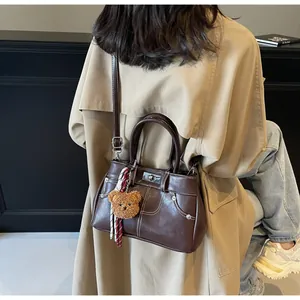 Détail du sac à main rétro marron foncé avec surpiqûres blanches et charme d'ours en peluche