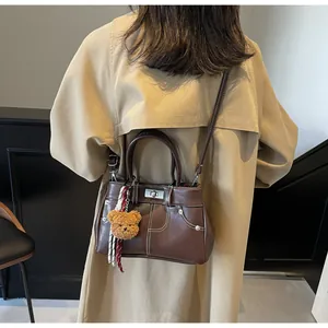 Détail d'un sac à main en cuir marron avec surpiqûres blanches et pendentif ours